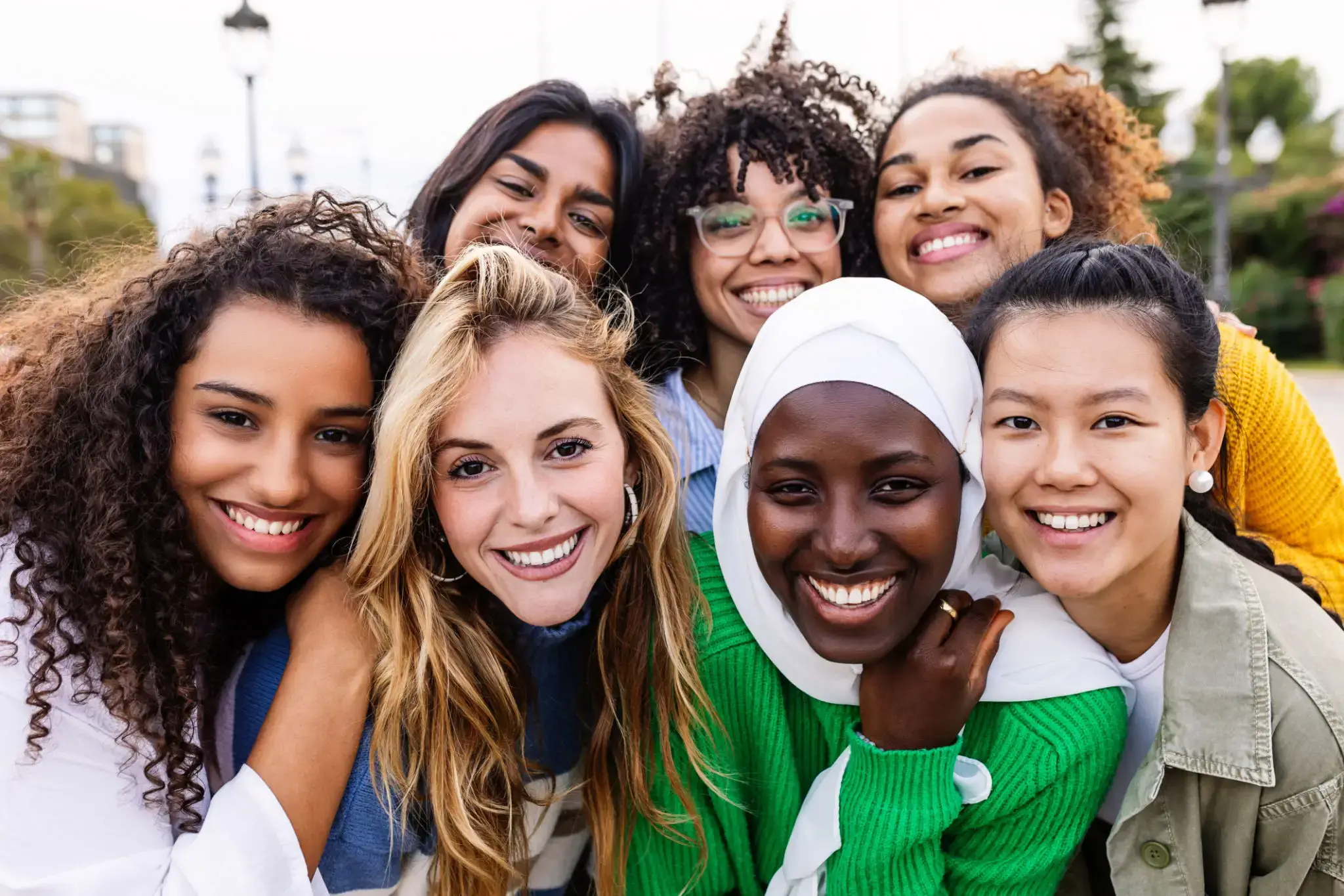 A diverse group of happy young women posing closely together outdoors.