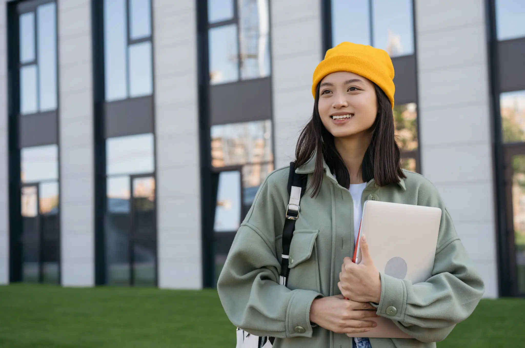 Young woman in a yellow beanie holding a laptop outdoors.